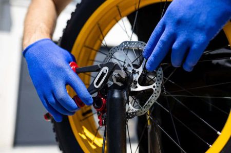 Technicus voert onderhoud uit aan de remschijf van een fatbike met blauwe handschoenen.